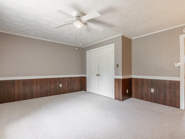 carpeted spare room featuring ceiling fan, crown molding, wooden walls, and a textured ceiling