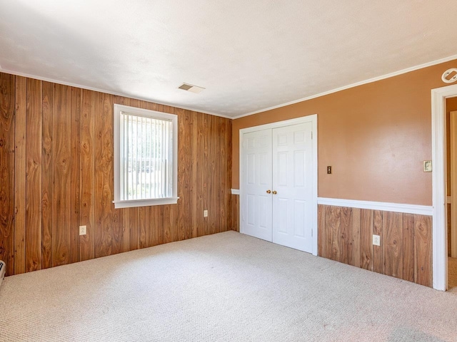 unfurnished bedroom featuring a closet, ornamental molding, wooden walls, and carpet