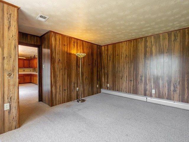 empty room featuring baseboard heating, a textured ceiling, light carpet, and wood walls