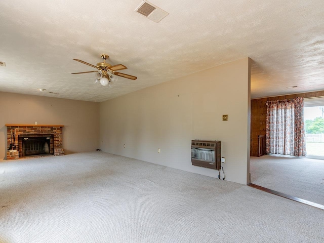 unfurnished living room with heating unit, a fireplace, carpet, ceiling fan, and a textured ceiling