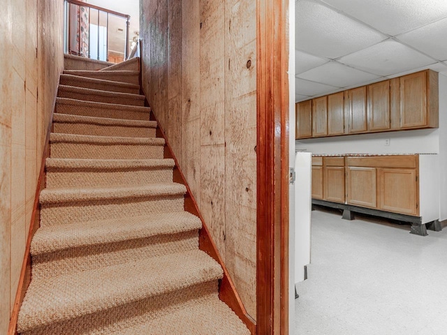 staircase featuring a drop ceiling and wood walls