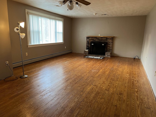 unfurnished living room with a fireplace, hardwood / wood-style flooring, a baseboard heating unit, ceiling fan, and a textured ceiling