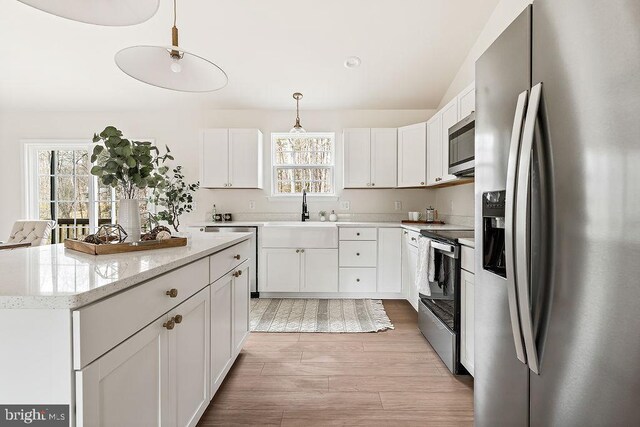 kitchen featuring a kitchen island, a sink, appliances with stainless steel finishes, pendant lighting, and white cabinetry