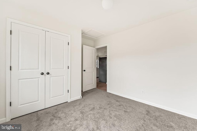 unfurnished bedroom featuring baseboards, carpet, attic access, freestanding refrigerator, and a closet