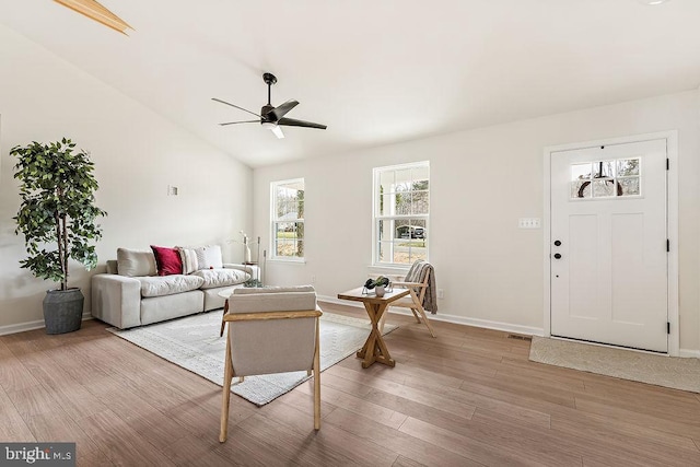 living room featuring baseboards, vaulted ceiling, a ceiling fan, and light wood finished floors