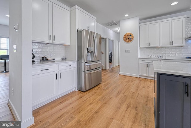 kitchen with white cabinetry, backsplash, stainless steel fridge, and light wood-type flooring