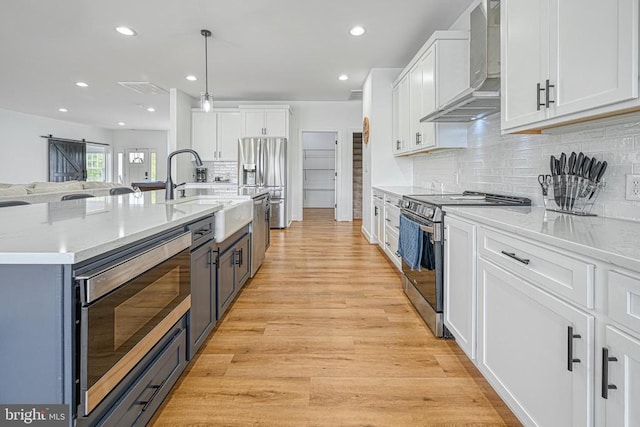 kitchen with pendant lighting, wall chimney range hood, sink, appliances with stainless steel finishes, and white cabinetry