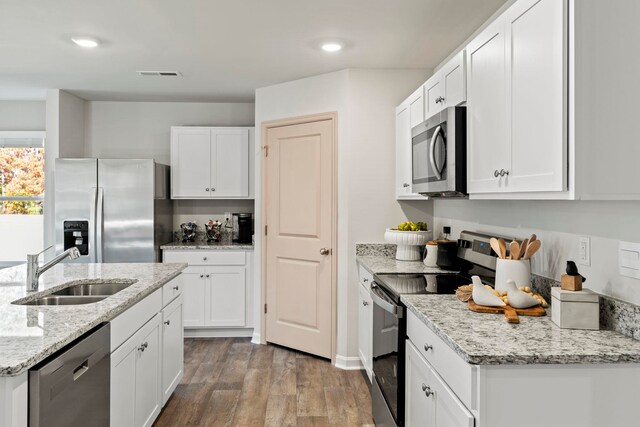 kitchen with sink, appliances with stainless steel finishes, white cabinetry, wood-type flooring, and light stone countertops