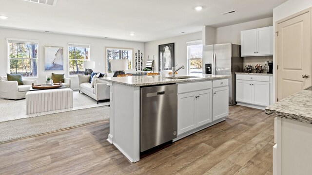 kitchen featuring sink, light hardwood / wood-style flooring, stainless steel appliances, white cabinets, and a center island with sink