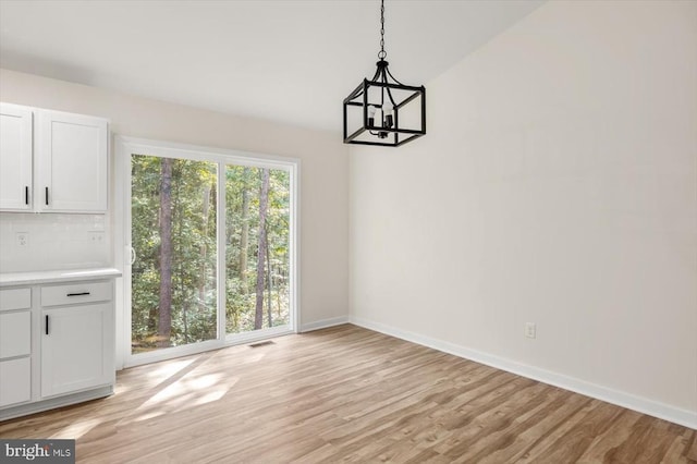 unfurnished dining area featuring a chandelier, light wood-type flooring, visible vents, and baseboards