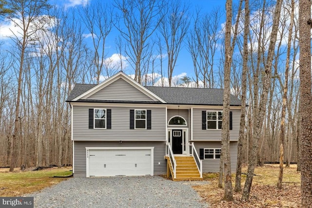 split foyer home featuring a garage, driveway, and roof with shingles