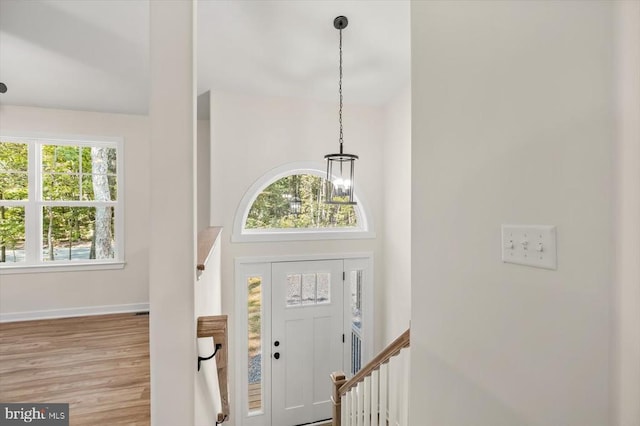 foyer entrance featuring light wood-style floors, a towering ceiling, baseboards, and an inviting chandelier