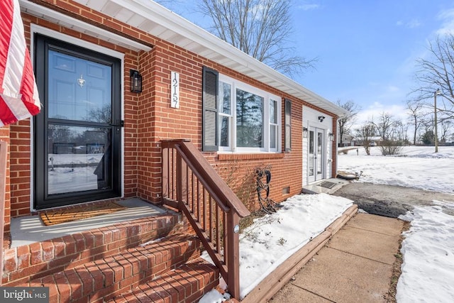 snow covered property entrance with crawl space and brick siding