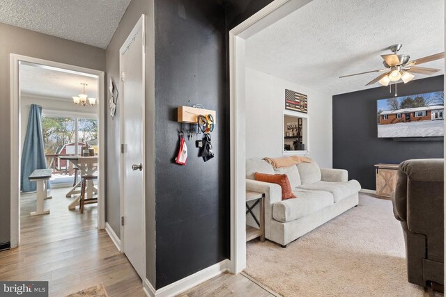 living area featuring a textured ceiling, ceiling fan with notable chandelier, wood finished floors, and baseboards