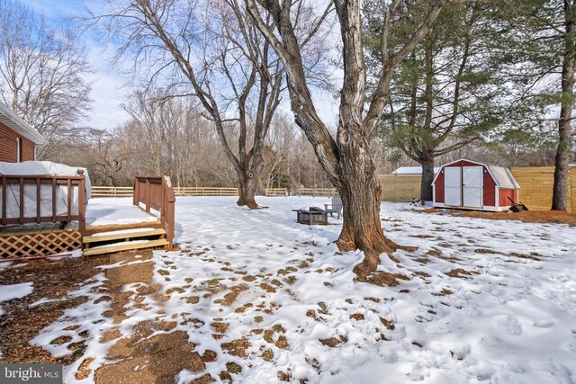 yard layered in snow with an outbuilding, fence, a deck, and a shed