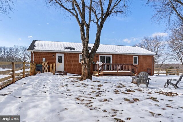 snow covered rear of property with a wooden deck, fence, and brick siding