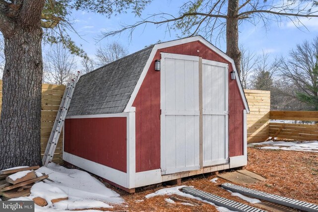 snow covered structure featuring a shed, fence, and an outdoor structure