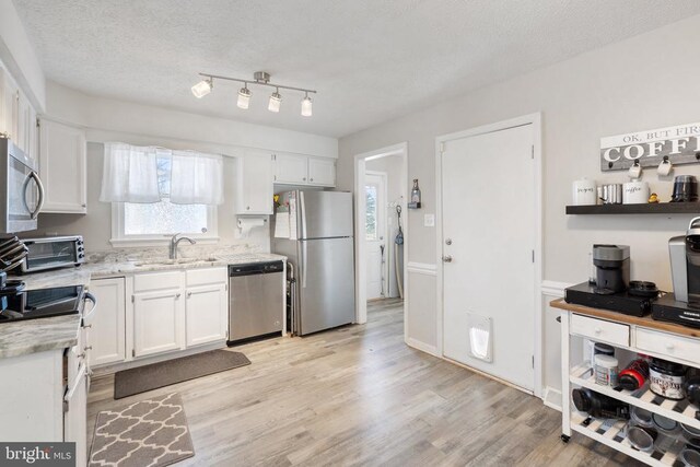 kitchen featuring appliances with stainless steel finishes, white cabinetry, a sink, and a textured ceiling