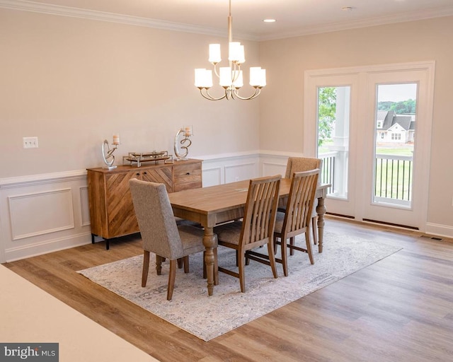 dining space with a wainscoted wall, a decorative wall, ornamental molding, wood finished floors, and a chandelier