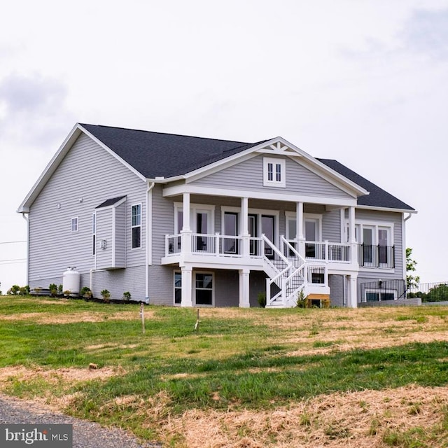 rear view of property featuring covered porch, a lawn, and stairs