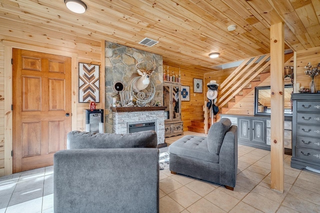 living room with light tile patterned flooring, a stone fireplace, wooden ceiling, and wood walls