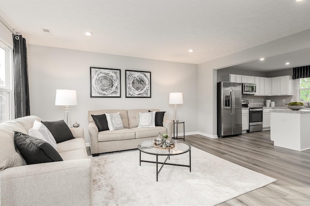 living room featuring visible vents, baseboards, wood finished floors, and recessed lighting