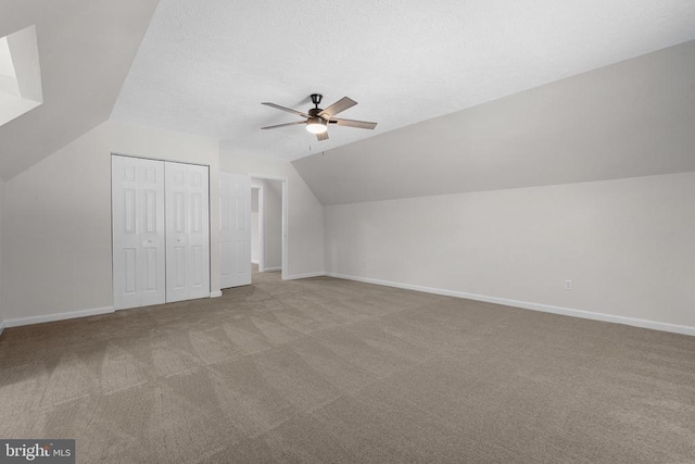 additional living space featuring a textured ceiling, carpet flooring, baseboards, ceiling fan, and vaulted ceiling