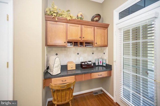 kitchen with dark countertops, dark wood-style flooring, backsplash, and built in study area