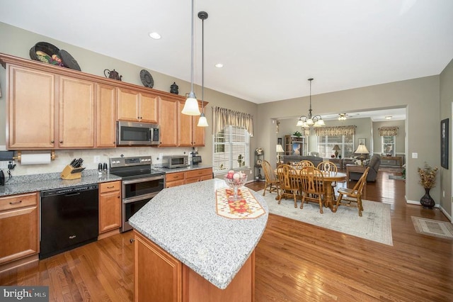 kitchen with light stone countertops, a kitchen island, hardwood / wood-style flooring, appliances with stainless steel finishes, and a chandelier