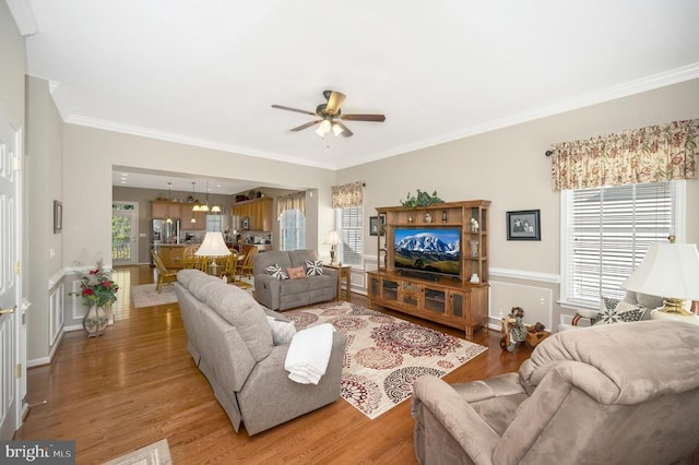 living area with light wood finished floors, a ceiling fan, and ornamental molding