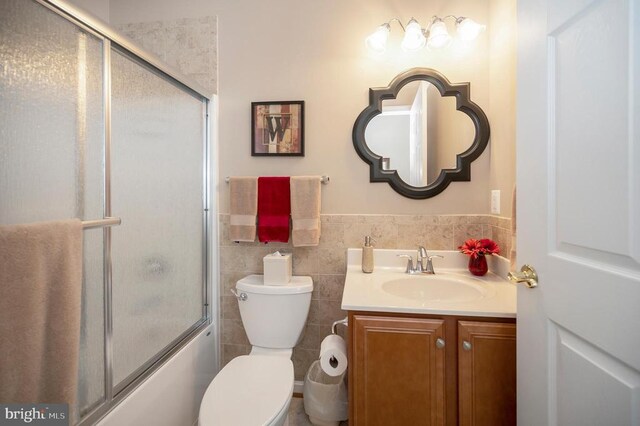 bathroom with vanity, tile walls, toilet, and enclosed tub / shower combo