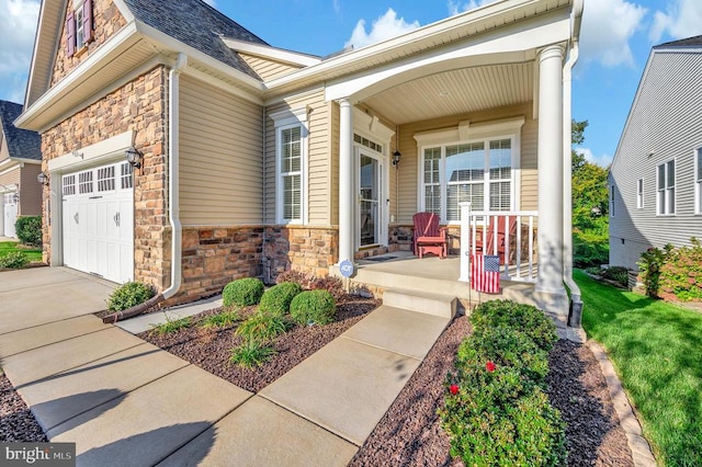 doorway to property featuring stone siding, covered porch, an attached garage, and roof with shingles