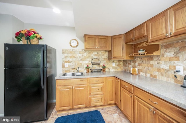 kitchen featuring light countertops, decorative backsplash, freestanding refrigerator, brown cabinetry, and a sink