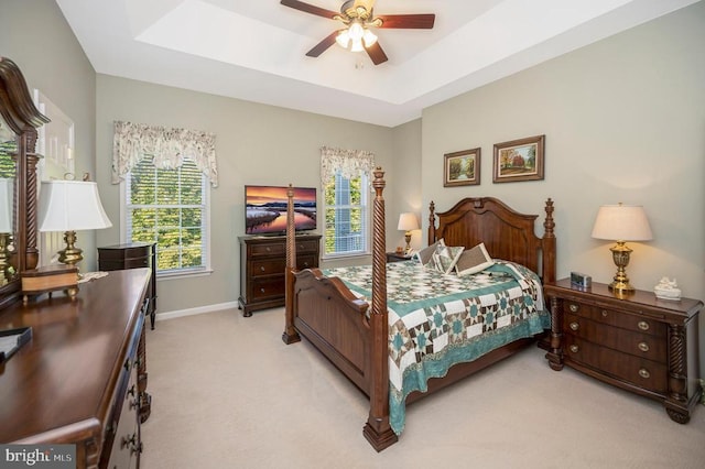 bedroom with light colored carpet, baseboards, a tray ceiling, and a ceiling fan