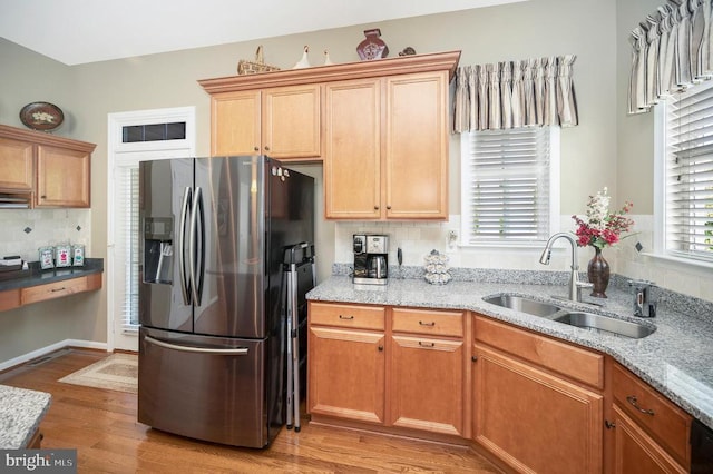 kitchen with light stone countertops, light wood-type flooring, stainless steel refrigerator with ice dispenser, and a sink