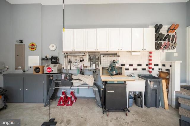 kitchen featuring electric panel, decorative backsplash, white cabinets, and concrete floors