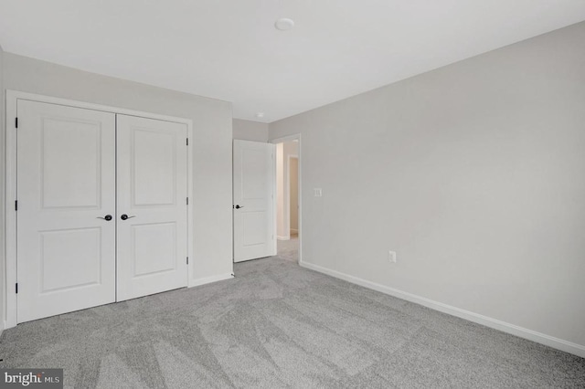 unfurnished bedroom with baseboards, a closet, and light colored carpet