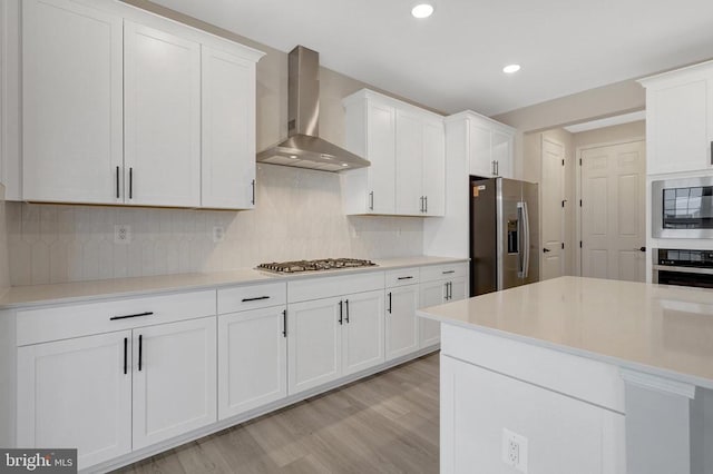 kitchen featuring white cabinets, wall chimney exhaust hood, stainless steel appliances, and light countertops