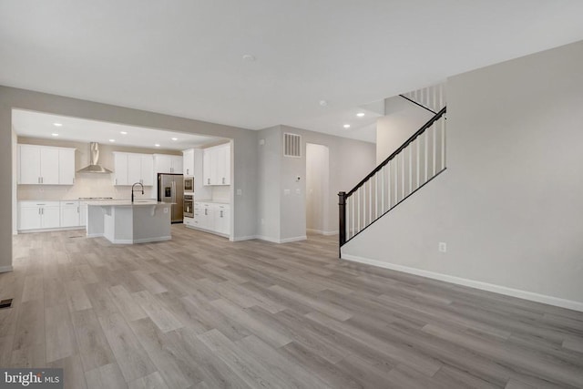 unfurnished living room featuring recessed lighting, stairway, light wood-type flooring, and baseboards