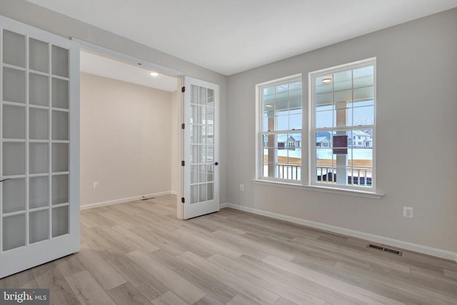 empty room with light wood finished floors, visible vents, baseboards, and french doors