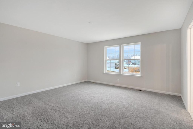 empty room featuring carpet floors, visible vents, and baseboards