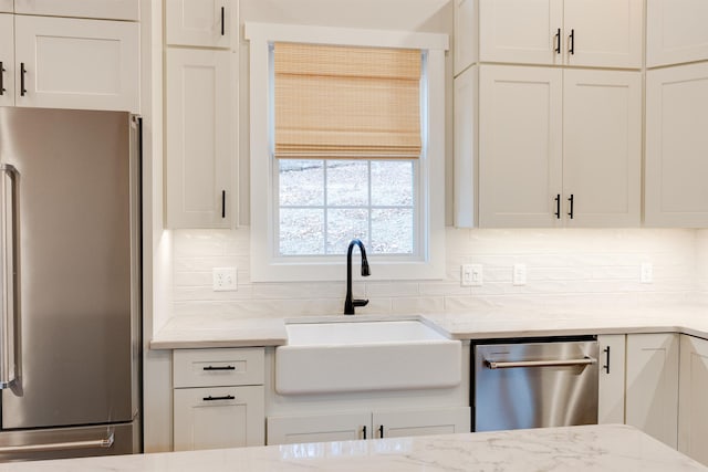 kitchen with sink, appliances with stainless steel finishes, light stone countertops, decorative backsplash, and white cabinets