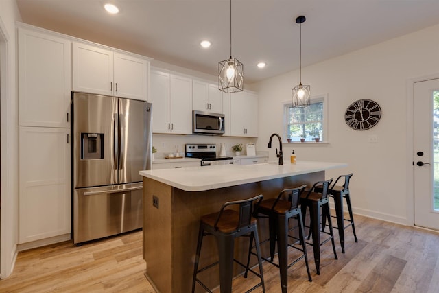 kitchen with appliances with stainless steel finishes, a breakfast bar, white cabinetry, an island with sink, and hanging light fixtures