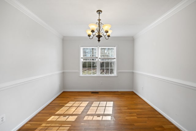 unfurnished dining area featuring baseboards, ornamental molding, wood finished floors, and a notable chandelier