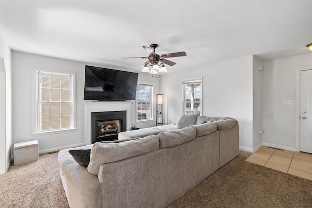 tiled living room featuring carpet floors, a fireplace, baseboards, and a ceiling fan