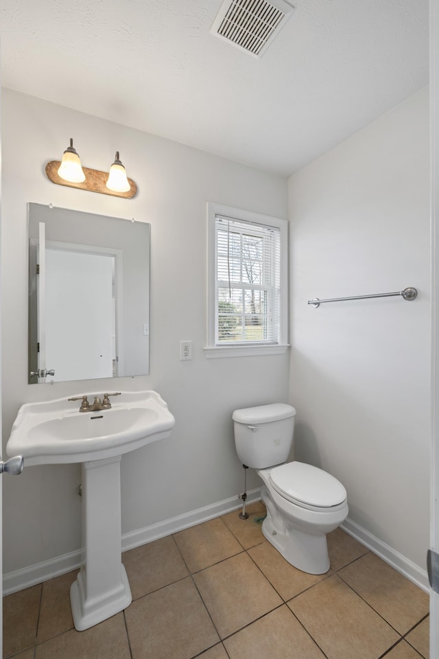 half bathroom featuring toilet, baseboards, visible vents, and tile patterned floors