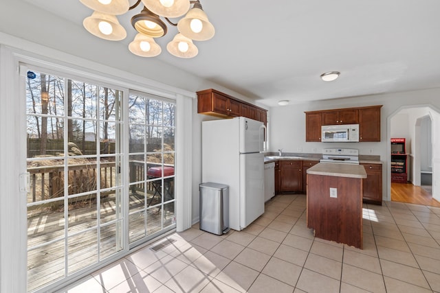 kitchen with a center island, arched walkways, light tile patterned floors, light countertops, and white appliances