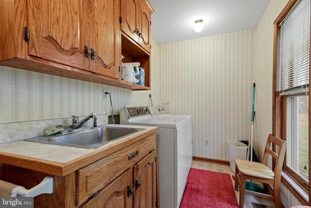 clothes washing area featuring separate washer and dryer, sink, light hardwood / wood-style floors, and cabinets