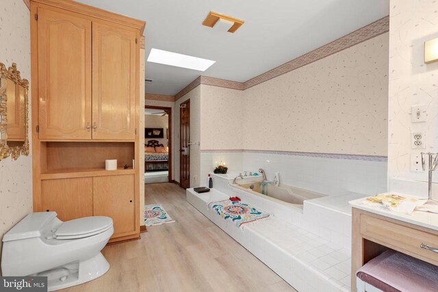 bathroom with hardwood / wood-style floors, a skylight, a bathing tub, vanity, and toilet