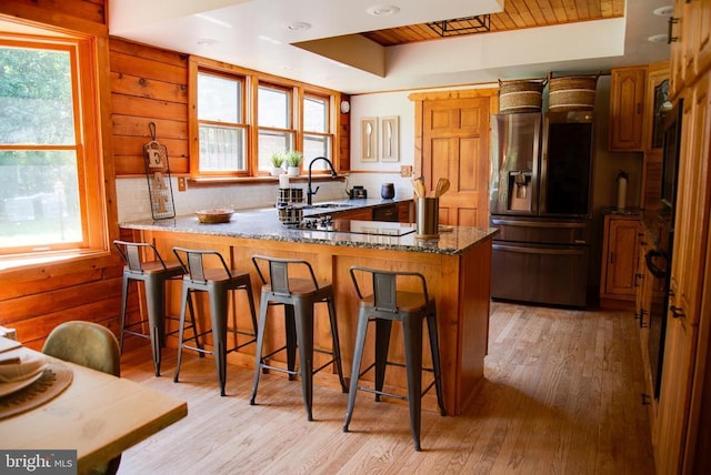 kitchen featuring stainless steel refrigerator with ice dispenser, a raised ceiling, a sink, dark stone counters, and a peninsula